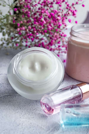 Composition of close-up care products for the skin of the face serum and cream, on a light marble background, pink flowers. Vertical photography.の写真素材