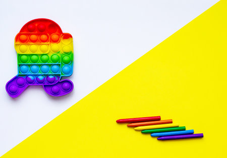 Push pop bubble flexible fidget sensory toy provide discharge and are good for the development of kids on white background. Colored pencils for drawing on a yellow table.の写真素材