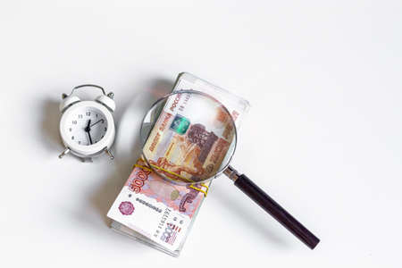 The concept of accumulating and investing money, currency rubles bills of five thousand through a magnifying glass, on a white background with a place for your text, white clock.の写真素材