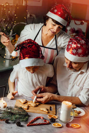 Vertical photography. Christmas family tradition, woman watching her grandson with grandpa prepare gingerbread in the kitchen.の写真素材