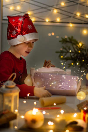 Christmas magic child boy in red hat tears off gifts, vertical photo.の写真素材