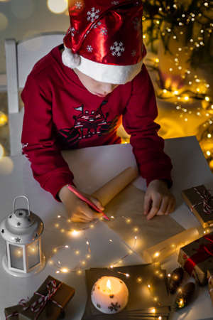 Vertical photo child boy in red christmas hat writing letter to Santa Claus.の写真素材