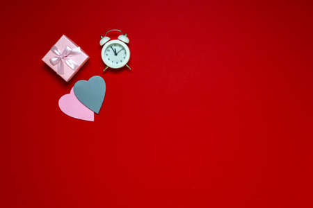 Flat lay on workspace time for valentine's day on red background, heart gifts and alarm clock, copy space.の写真素材