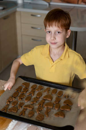 Child red-haired boy hold a tray with cookies in the form of a bunny, rabbit and others for Easter,...