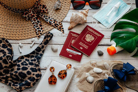 Flat lay of accessories for summer beach holiday during covid-19 pandemic: passport, swimsuit, hat,...