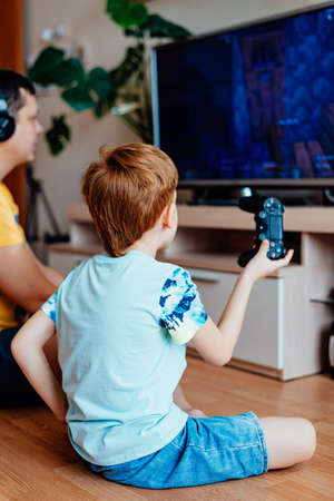 Leisure and entertainment. time together. Father in headphones and son red-haired boy play video...
