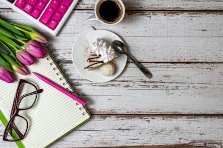 Flat lay view of desktop surface tulips coffee with cake and notepad with calculator on wooden light...