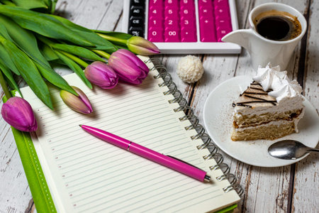 view of desktop surface tulips coffee with cake and notepad with calculator on wooden light background close-up, holiday in financial sphere.の写真素材