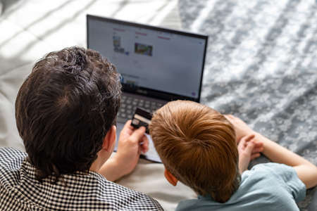 Young father and son shopping online together, family time. Child red-haired boy and dad at the laptop choose purchases, rear view.の写真素材