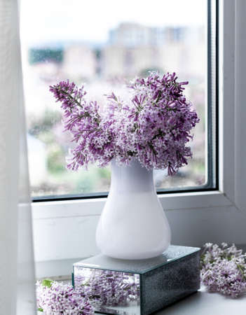 Still life on the windowsill blooming lilac in a white vase. Spring flowers, vintage style.