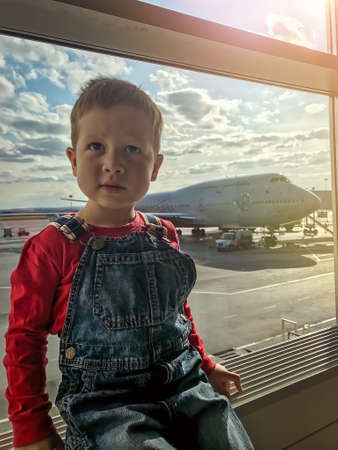 A small boy is waiting to board a flight in the airport transit hall and is sitting by the window...