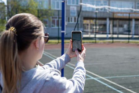 Young blonde woman in sportswear is resting after playing sports, running in the stadium, taking pictures on the phone.の写真素材