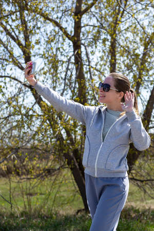 A young girl in sportswear after a run in the park is resting taking a selfie on the phone or chatting in a video chat.の写真素材