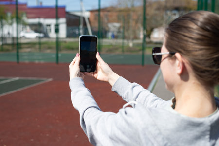Young blonde woman in sportswear is resting after doing sports, running in the stadium, taking pictures on the phone, back view.の写真素材