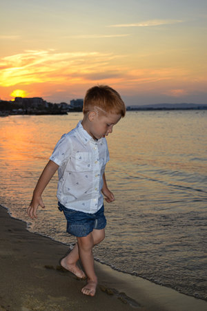 Life style happy childhood, child redhead little boy walking on the beach by the sea at sunset, beautiful coast in Bulgaria.の写真素材