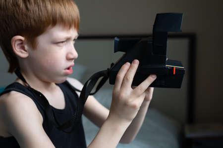 Child red-haired boy holding an old retro camera in his hands, children's hobby photography, life style portrait.の写真素材
