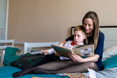 Cheerful mother hugging son and reading handmade greeting card with heart while resting on bed during holiday celebration mothers day at home.の写真素材