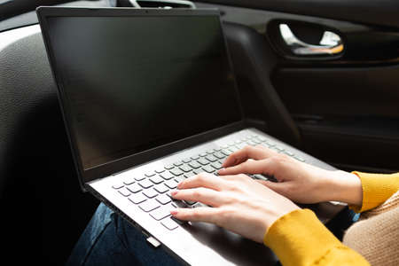 Hands in the frame typing text on a laptop while sitting in a car, freelancer or blogger at work,...