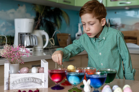 A beautiful red-haired boy paints eggs in the kitchen for Easter. Emotions of surprise....
