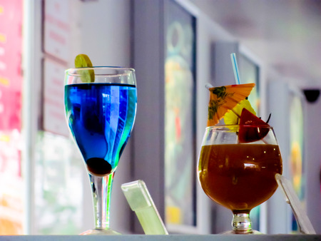 blue drink in a tall glass and red drink in a stout glass placed on a counter with a rate card  The drinks are decorated with lime wedges and an umbrellaの写真素材