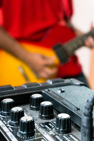 Amplifier for an electric guitar showing all the knobs for special effects, tone etc  The musician playing the guitar in soft focus in the backgroundの写真素材