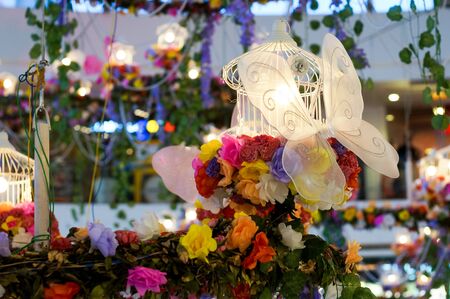 Artificial decorations in a building with colorful flowers, white butterfly and lights. Celebrating the joy and happiness of springの写真素材