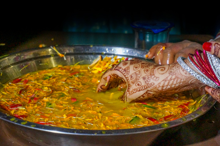 Indian bride soaking hands in turmeric water and flower petals as part of a ritual. This is a traditional ceremony in North indian weddingsの写真素材
