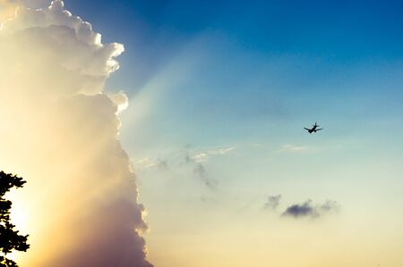 aeroplane flying near a cloud with sun rays from setting sun streaming on it. Useful for travel or vacation related imageryの写真素材