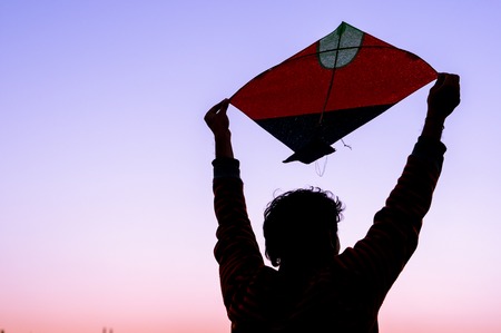 boy holding a paper kite above his head at dusk. Silhouette shows the kites flown during makar sankranti, independence day and uttarayan kite festivalの写真素材
