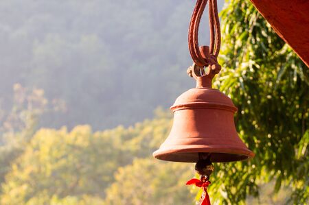 Hindu prayer bells in a remote temple in the forest with the bokeh of the trees and golden sunlight from a morning sunの写真素材