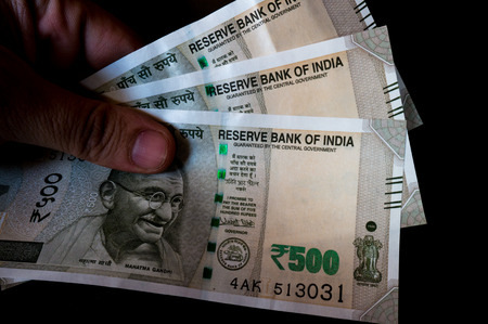 Person holding the new indian Rs 500 note isolated on black. These new currency notes have been...