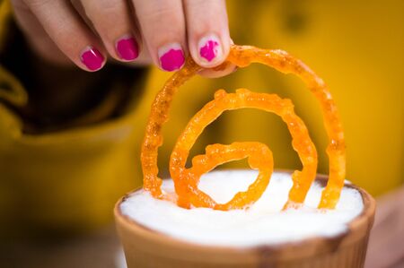 Jalebi being dipped in a earthenware milk cup by a lady in yellow. Jalebi is a very popular indian dish eaten alone or with milkの写真素材
