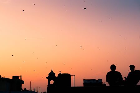 Silhouette of people flying kites at sunset in Jaipur on Makar Sankranti. The sky is filled with kitesの写真素材