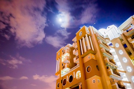 Modern skyscraper set against a moonlit cloudy monsoon sky in Delhi. Apartment buildings like this are getting very popular as the population increasesの写真素材