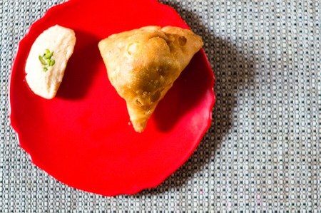 Samosa, peda barfi on red plate and woven mat, typical indian snack breakfast