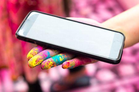 Colorful hand on holi holding a mobile phone depicting technology and tradition on holi