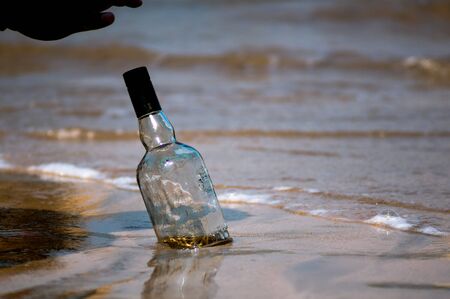 Upturned glass bottle buried in the sand with waves, surf and sand in the background at Diu beach Gujarat India. Shows the place where most of gujarat comes to consume alcohol given gujarat is a dry state. Can show the thrash on the beach or a party in progressの写真素材