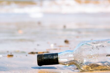 Upturned glass bottle buried in the sand with waves, surf and sand in the background at Diu beach...