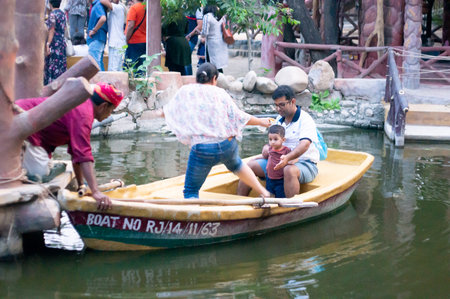 Traditionally dressed rajasthani boatsman holding a boat while tourists visitors climb on it for a boat ride on a lakeのeditorial素材