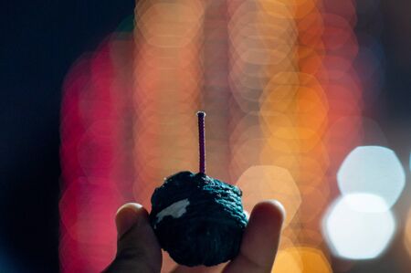 Human hand holding green sutli rassi bomb in front of out of focus lights with a hexagon bokehの写真素材