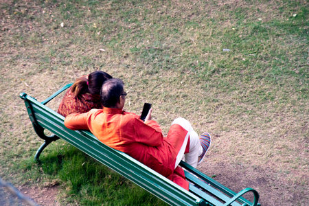 Cheerful traditional indian old couple sitting on a park bench enjoying content on mobileのeditorial素材
