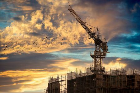 Crane on top of an under construction building shot against the orange skies of dusk. The framework of the building is exposed and the construction crane is clearly visibleの写真素材
