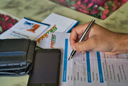Gurgaon - India, Circa 2019: Photograph of Fast Tag application form being filled with a fountain pen, along with a wallet and a mobile phone on a beautifully decorated table. Fast tag is expected to make toll stops cash and hassle free and was implementeのeditorial素材