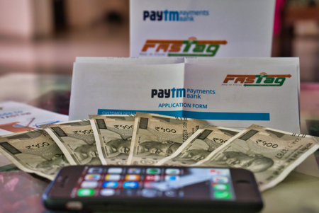 Gurgaon - India, Circa 2019: Photograph of Fast Tag on a beautifully crafted table along with currency notes, the application form provided by PayTM payment bank and a mobile phone. Fast tag is expected to make toll stops cash and hassle free and was implのeditorial素材