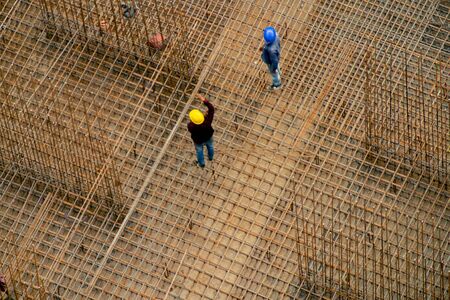 Construction workers in India standing on a rebar reinforcing bar platform making a pillar. Shot with an aerial view it shows the preparation work for pouring concrete to construct a skyscraperの素材 [FY310139210254]