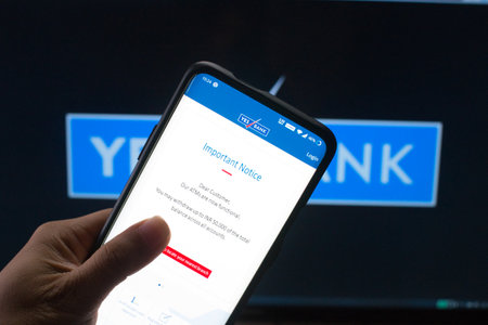Jaipur, India, Circa 2020 - A mobile logged into the yes bank mobile application infront of the yes bank board. The background board is brightly lit. The screen shows the new limits the RBI has put on the defaulting bankのeditorial素材