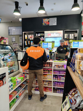 Swiggy store delivery agent standing at the counter of a departmental store collecting an order for...