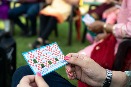 Selective focus shot of hands tolding tambola bingo housie tickets with some numbers folded and people in the backgroundのeditorial素材