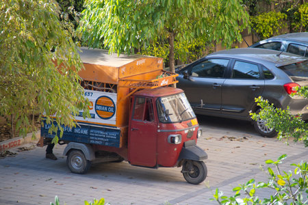 Delhi, India - circa 2020 : Auto rickshaw with Indane cooking gase from Indian oil marked on the sides parked in the middle of some trees while the driver makes home deliveries of gas cylinders used for cookingのeditorial素材