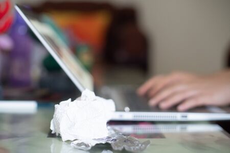 Young indian woman working on a laptop while sick with white tissues and medicine in silver foil nearby while she types in the background working on a project to safegurard her job and livelihoodの写真素材